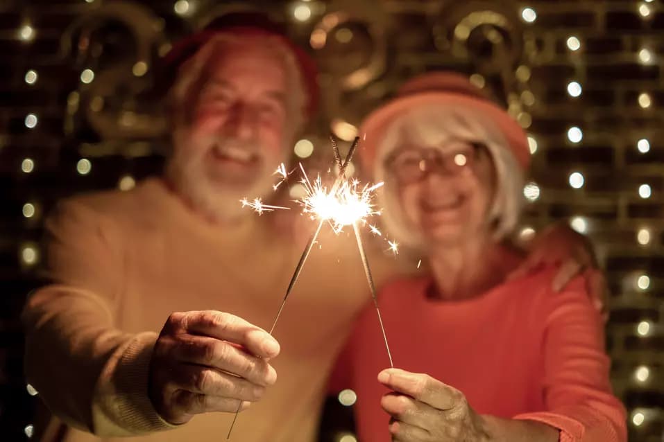 Blurred caucasian senior couple holding sparklers celebrating new year. Happy lifestyle for mature retirees, party lights