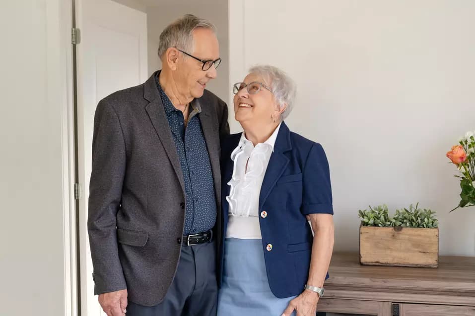 Happy senior couple hugging each other and standing in a suite / Couple âgé heureux s'étreignant et debout dans une suite