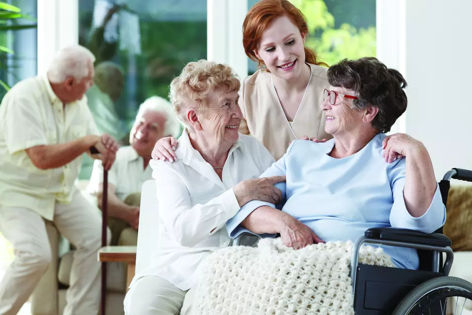 Gently smiling care giver having a light conversation with senior ladies / Une aide-soignante souriante discutant tranquillement avec des dames âgées