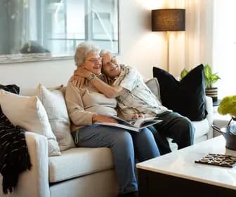 Joyful senior couple sitting on couch while hugging/holding each other / Un couple de personnes âgées rayonnant de joie, assis sur un canapé, enlacés