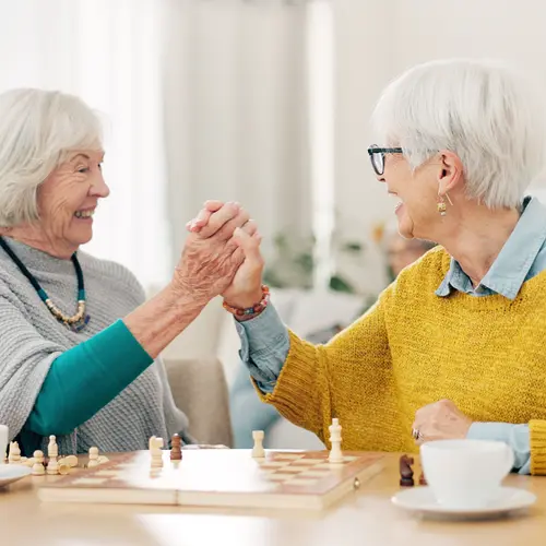 Senior woman, friends and high five for chess match, game or winning on table together at home. Happy elderly women in celebration, playing strategic board game for victory or checkmate in retirement.