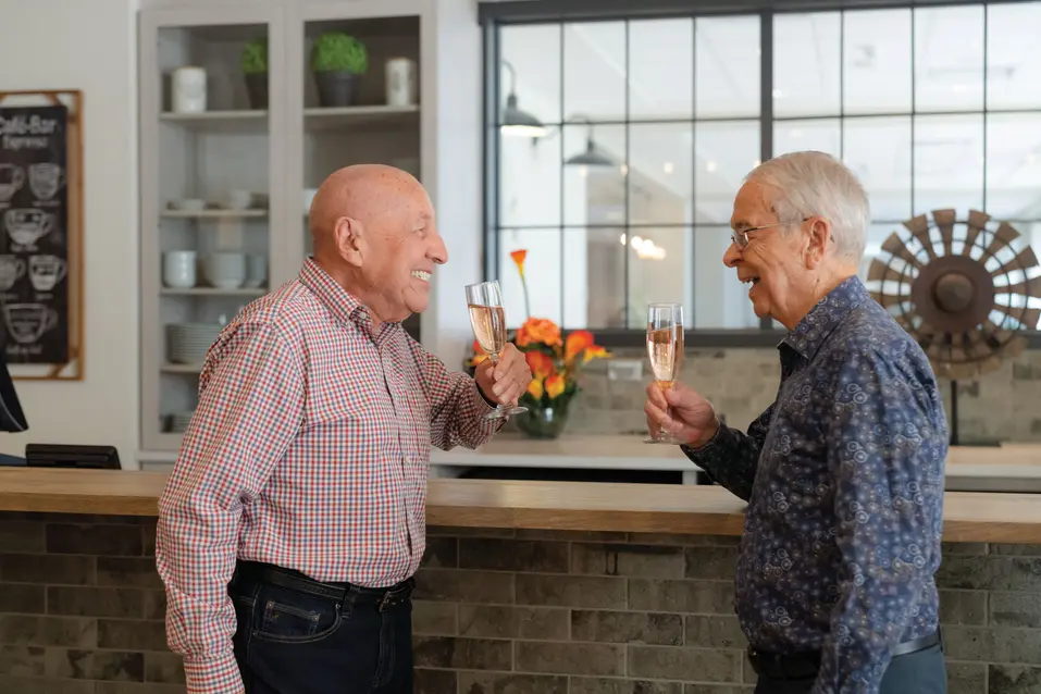 Senior men are having a joyful conversation while holding a champaign glasses in their hands / Des hommes âgés discutent joyeusement en tenant un verre de champagne à la main.