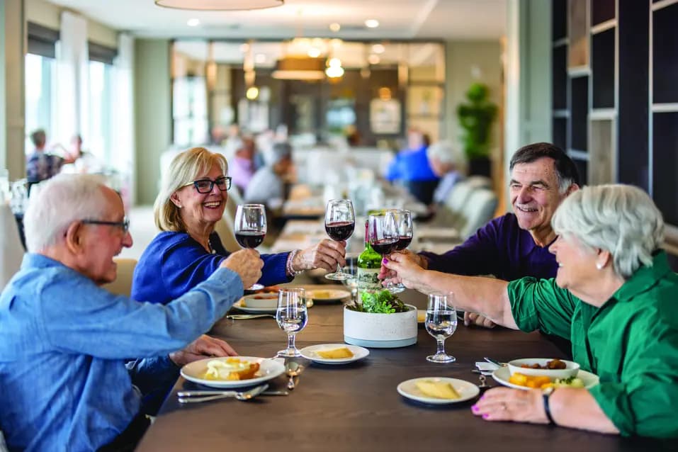 Seniors toasting with wine sitting around a dinner table in a public dining area