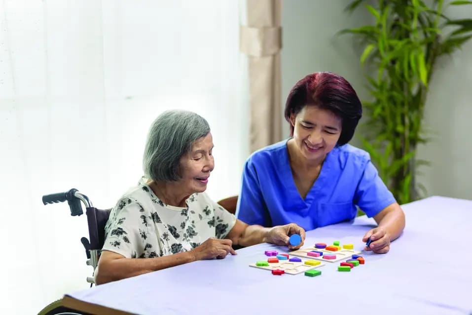Care giver and senior woman are working together to solve dementia prevention wooden puzzle / Une aide-soignante et une femme âgée travaillent ensemble pour résoudre un puzzle en bois sur la prévention de la démence