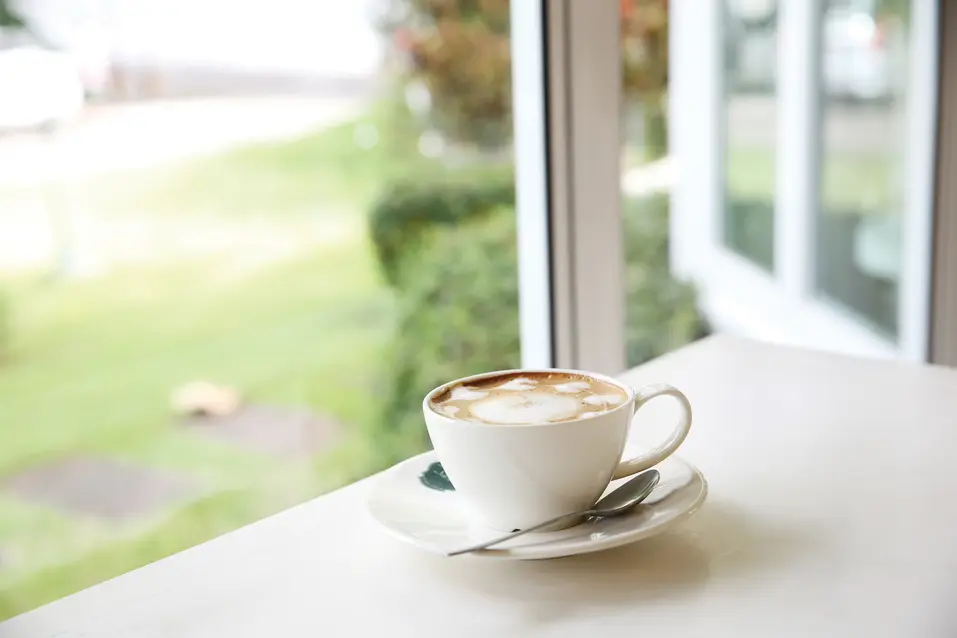 A cup of coffee with milk foam besides large window / Une tasse de café avec de la mousse de lait près d'une grande fenêtre