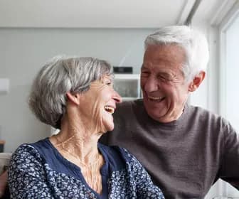 Senior couple in a couch happily laughing while looking into each others' eye / Couple de seniors dans un canapé, riant joyeusement en se regardant dans les yeux