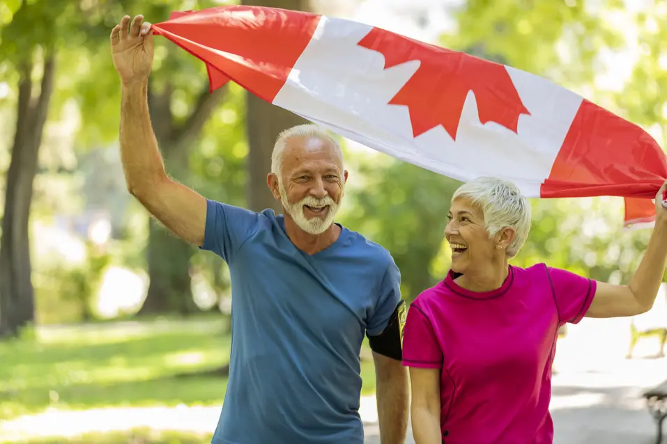 Senior couple is holding Canadian flag up in the air / Un couple d'aînés tient le drapeau canadien en l'air.