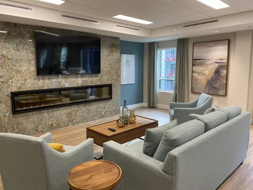 Cozy lounge with fireplace feature wall and seating at Chartwell Riverstone / Salon chaleureux avec mur de foyer et sièges à Chartwell Riverstone