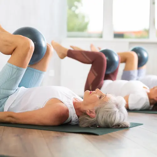 Active senior women doing pilates with soft ball lying on back in gym
