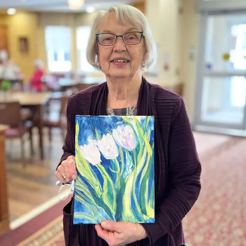 senior woman smiling at the camera holding a painting she created.