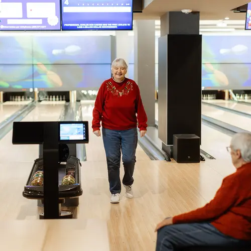 Happy senior couple bowling together in red sweaters / Un couple de seniors rayonnant de bonheur, jouant au bowling ensemble, vêtus de pulls rouges