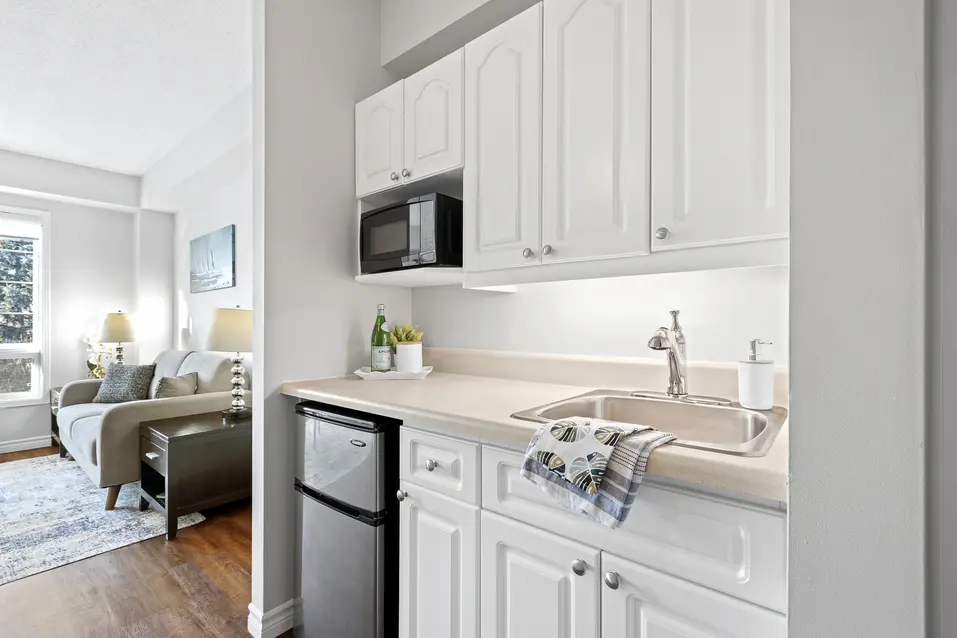 Compact kitchenette with white cabinets and stainless mini-fridge at Chartwell Empress Kanata / Kitchenette compacte avec armoires blanches et mini-réfrigérateur en acier inoxydable à Chartwell Empress Kanata