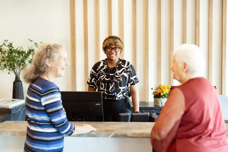 Senior friends talking to attendant in lobby, asking question / Des personnes âgées discutent avec un membre du personnel dans le hall et lui