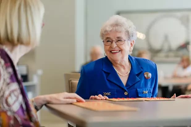 Senior woman residence at Chartwell retirement residence is smiling brightly while playing the bingo with her friend / Une femme âgée résidant à la résidence de retraite Chartwell affiche un sourire radieux alors qu'elle joue au bingo avec son amie