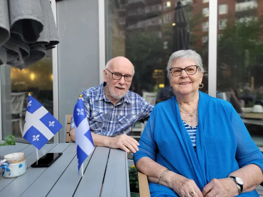 Residents sitting outdoors at a table with Quebec flags / Résidents assis à une table extérieure avec des drapeaux du Québec