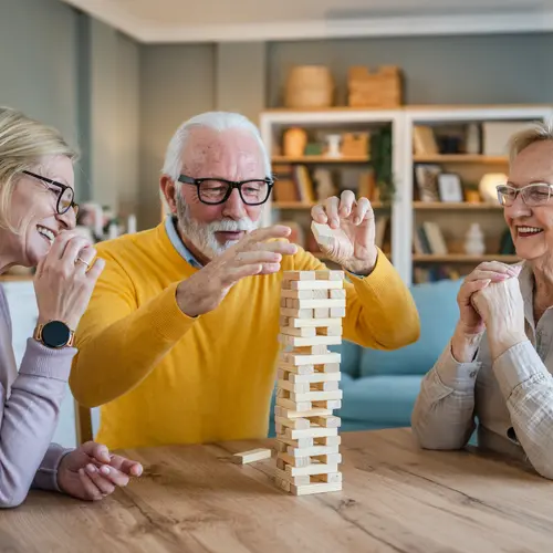 Group of senior people man and woman husband and wife friends or family play leisure board game at home have fun pensioner grandfather and grandmother spend time together with their mature daughter