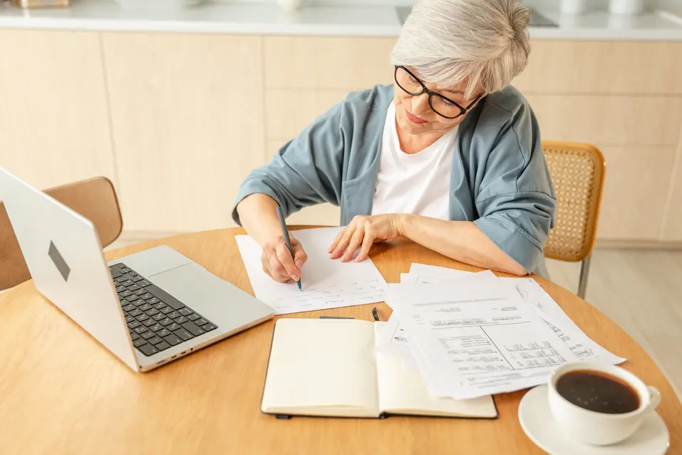 Senior woman taking a note for budget while having a cup of coffee / Une femme âgée prend des notes pour son budget tout en buvant une tasse de café