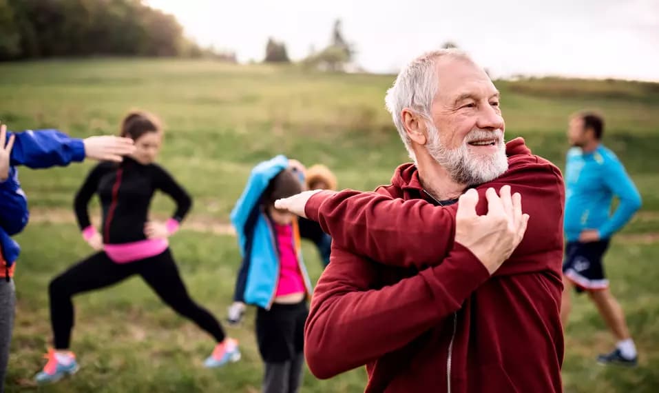 Senior man in wearing red hood, stretching out on a grass field / Homme âgé portant une cagoule rouge, s'étirant sur un champ d'herbe
