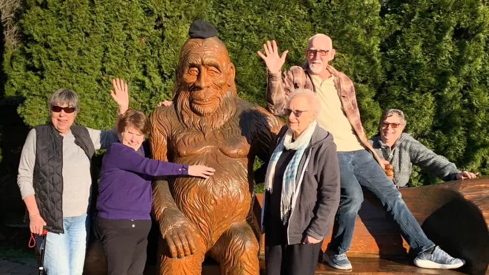 Residents posing around a large wooden statue outdoors / Résidents posant autour d’une grande statue en bois à l’extérieur