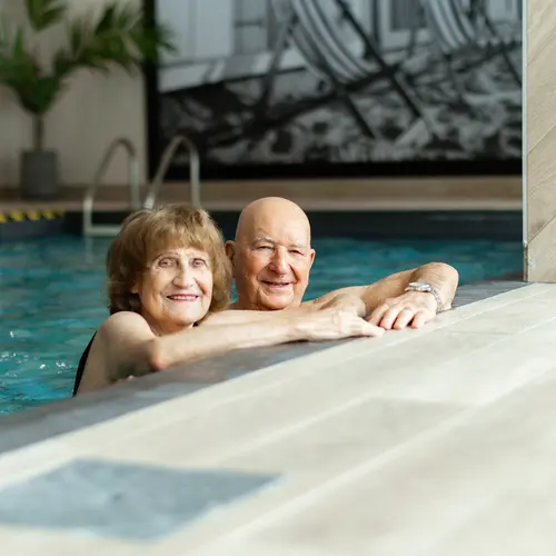 Happy senior couple in pool together while looking at camera