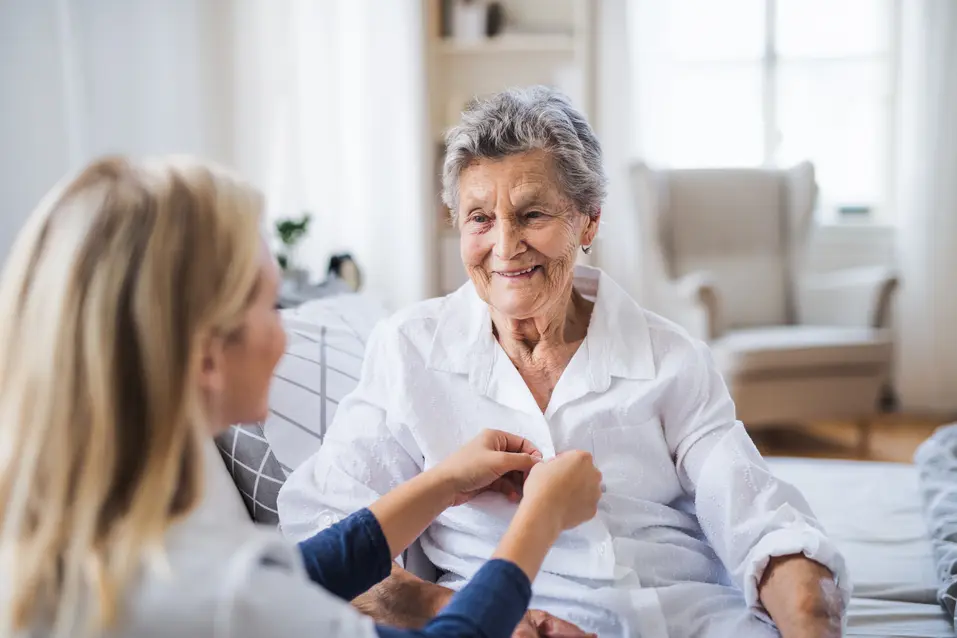 Care giver is helping a senior woman wearing her cloth / Une aide-soignante aide une femme âgée à s'habiller