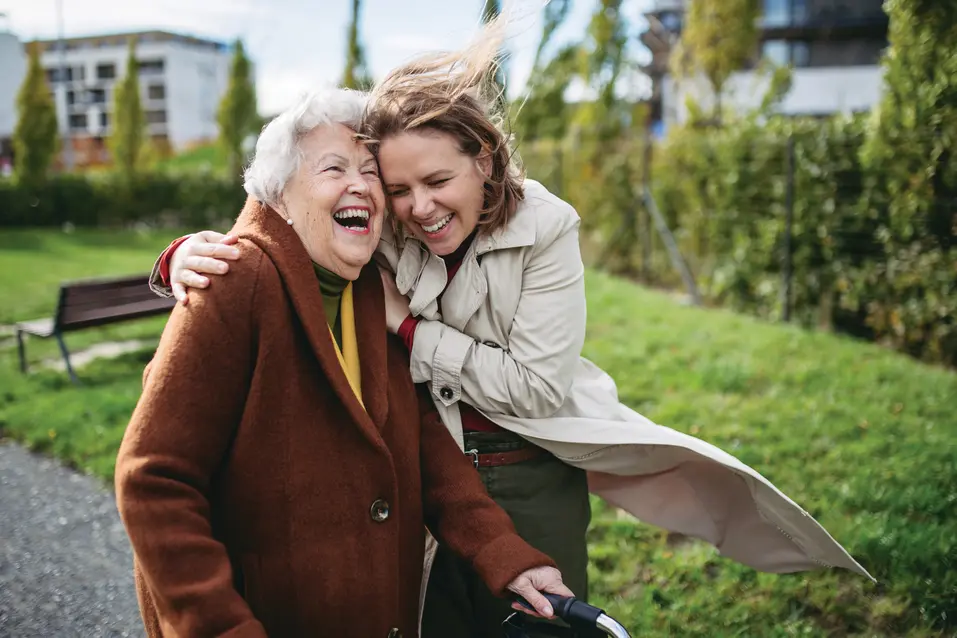 Senior woman and her adult daughter smiling big while having a walk during a windy day / Une femme âgée et sa fille adulte sourient largement pendant une promenade par une journée venteuse