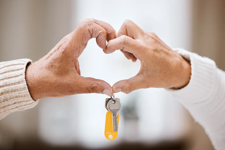 Senior couple making a heart sign with their hands and key / Couple âgé formant un cœur avec leurs mains et une clé