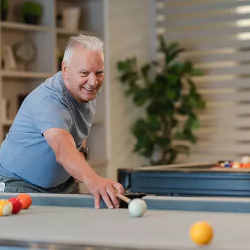 Senior resident enjoying the game of billiards in the activity room / Un résident senior s'adonne au billard dans la salle d'activités