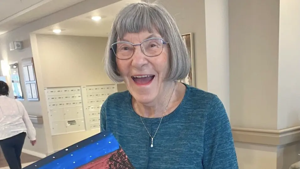 Resident holding a colourful landscape painting / Résidente tenant une peinture de paysage colorée
