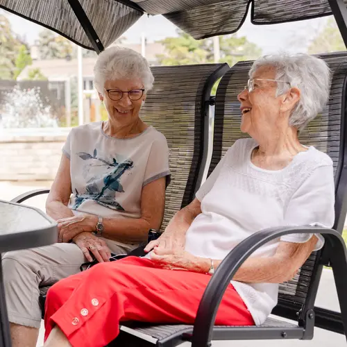 Two senior women are sitting on a swing chair and having fun conversation / Deux femmes âgées sont assises sur une balançoire et ont une conversation amusante