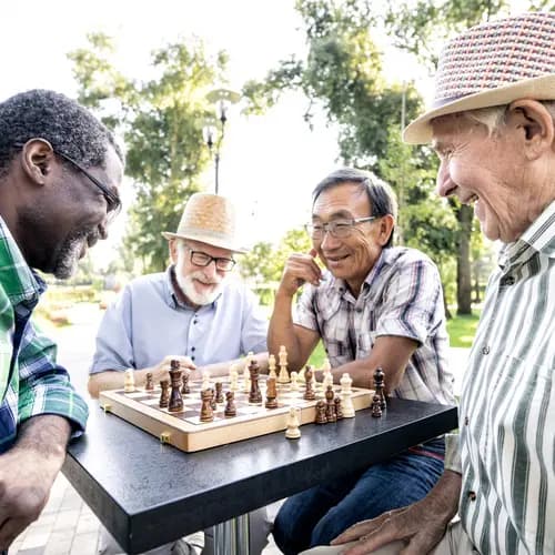 4 men sitting around a table outside smiling and playing chess.