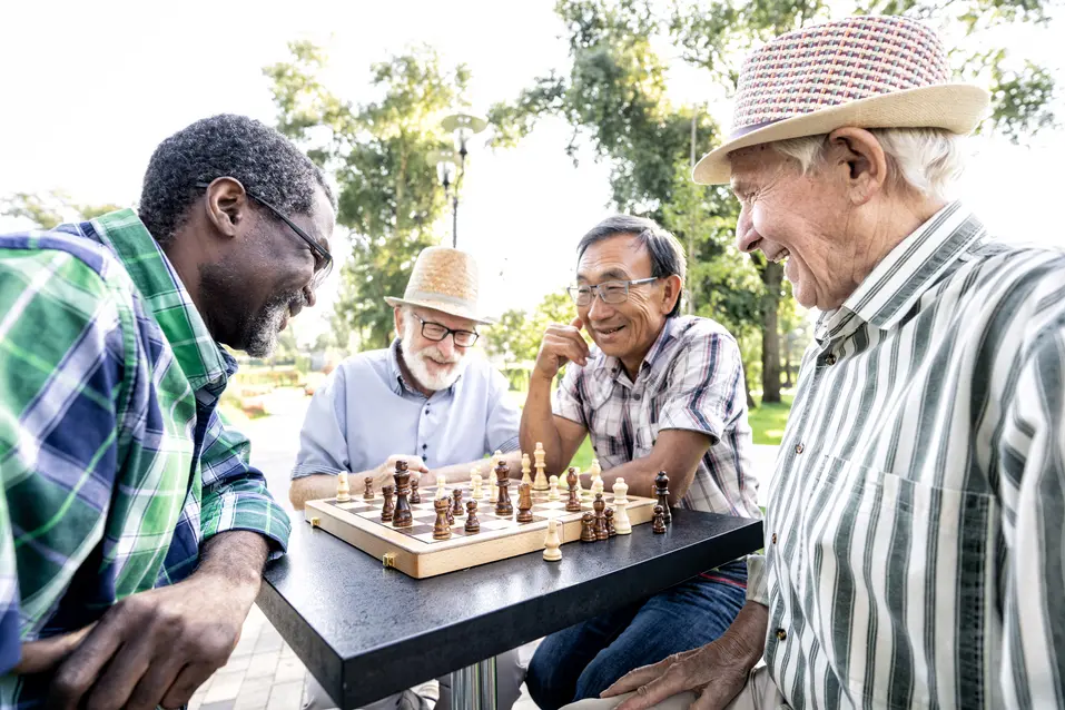 4mensittingaroundatableoutsidesmilingandplayingchess.