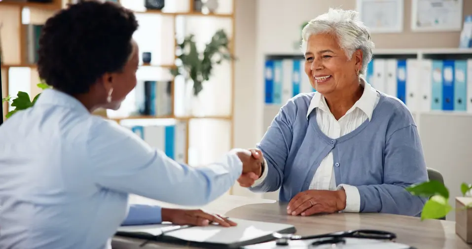 Senior woman is shaking hands with a sale person at an office / Une femme âgée serre la main d'un vendeur dans un bureau.