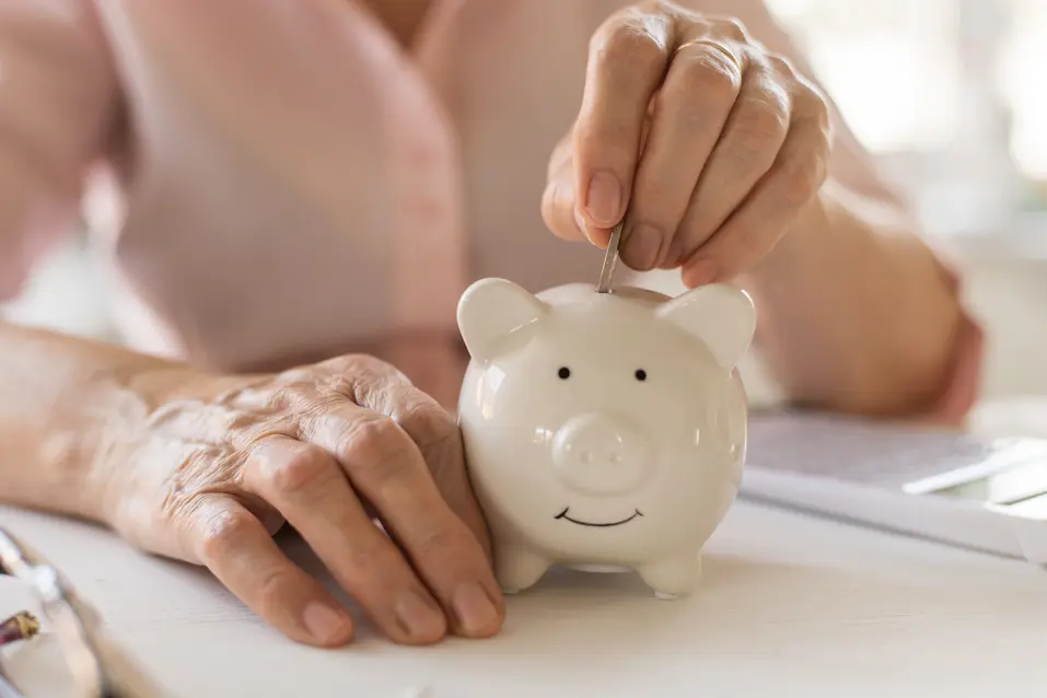 Putting a coin into a white piggy bank / Mettre une pièce dans une tirelire blanche en forme de cochon