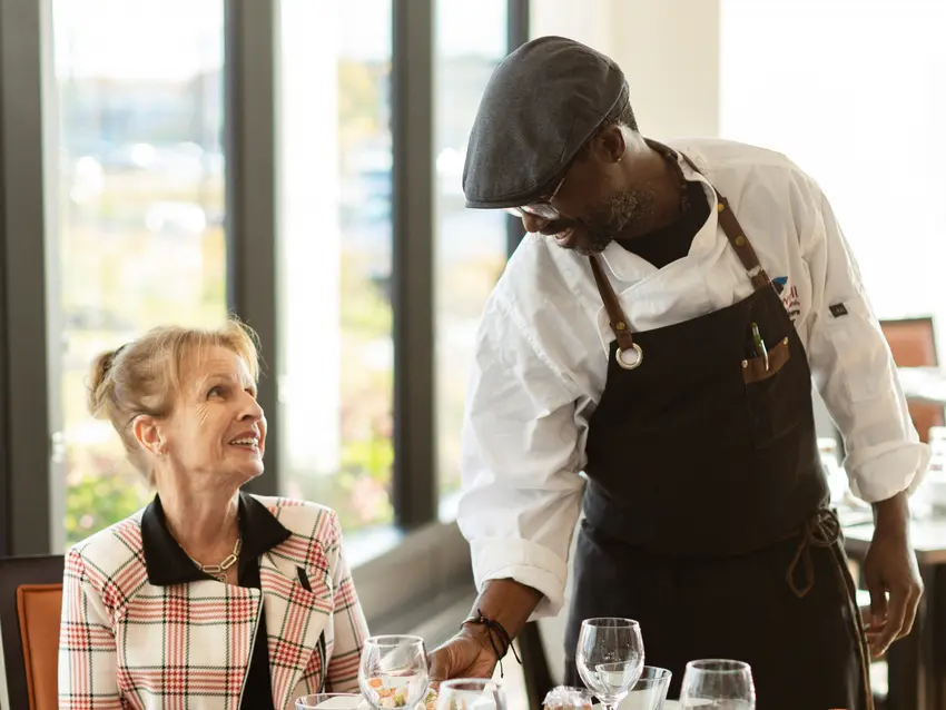 Senior woman at dinner table with server /Une femme âgée à table avec un serveur
