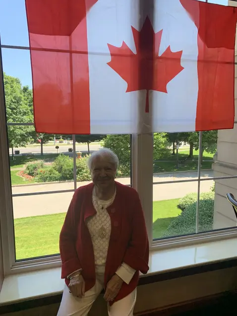 Resident at Chartwell Terrace on Square smiling and sitting under the Canadian flag / Résident de Chartwell Terrace on Square souriant et assis sous le drapeau canadien
