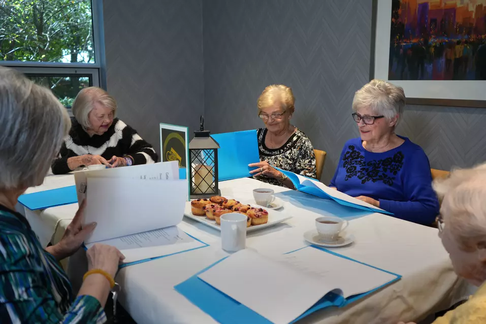 Group of residents sitting at a table reviewing binders during an indoor activity with coffee and pastries / Groupe de résidents assis à une table examinant des cartables lors d’une activité intérieure avec café et pâtisseries