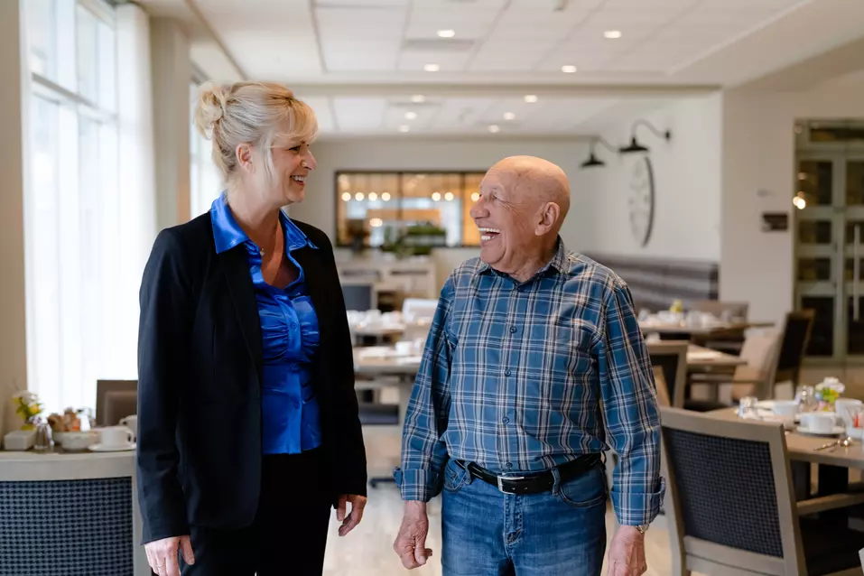 woman in black suit and blue shirt standing next to laughing senior man in plaid shirt and jeans