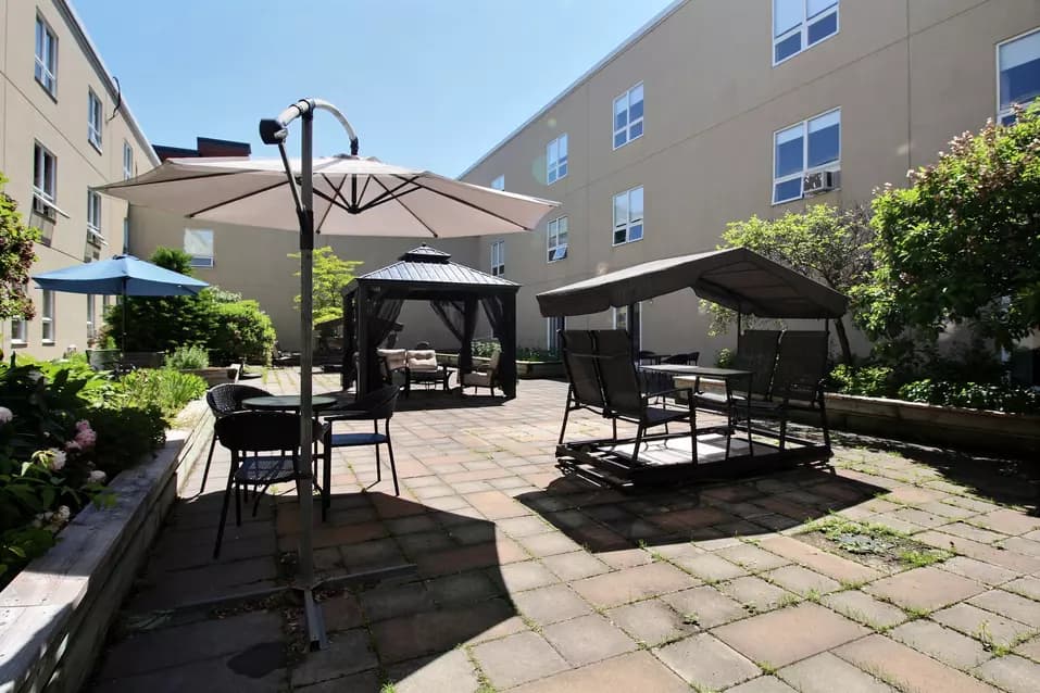 Cour intérieure extérieure avec balançoires table et parasols Chartwell Domaine Notre-Dame résidence pour retraités retirement residence Exterior courtyard with swigns and parasol