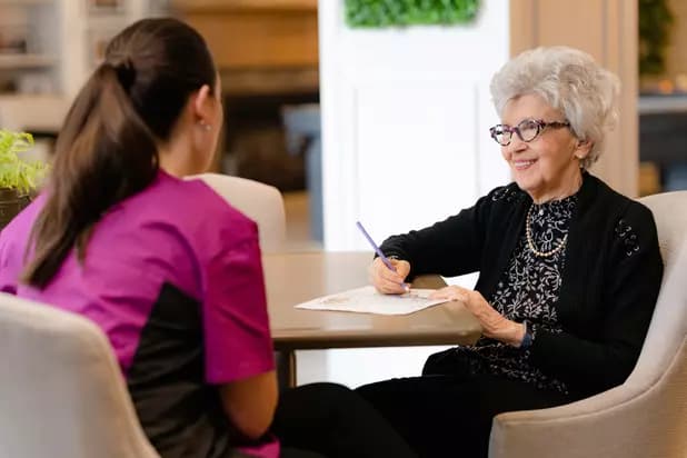 Chartwell Memory Care employee chatting with the senior lady colouring