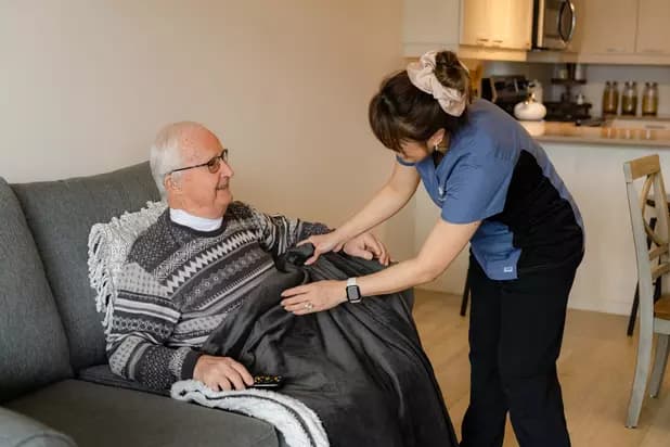 Chartwell Care employee helping the senior resident cover blanket over him