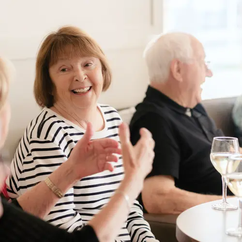 Senior resident at Chartwell is smiling while having a joyful social conversation with her fellow residents / Une résidente âgée de Chartwell sourit tout en ayant une conversation sociale joyeuse avec ses compagnons de résidence