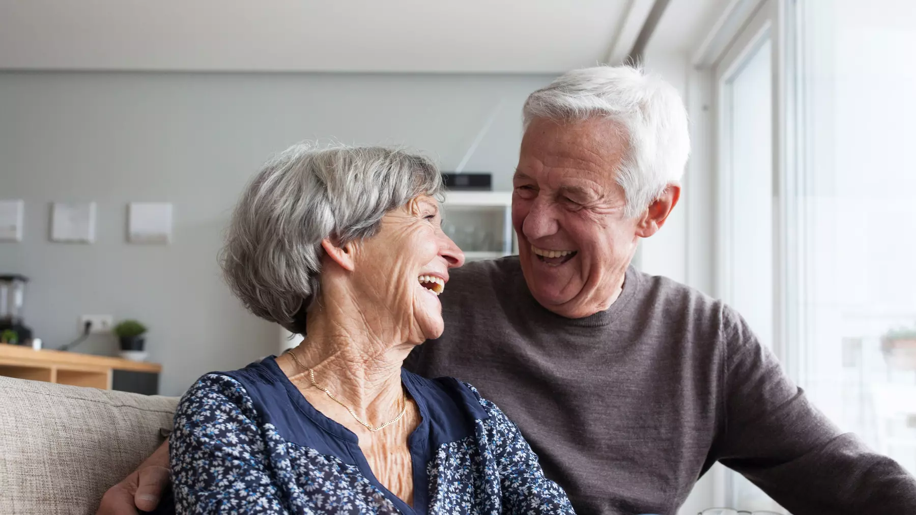 Senior couple in a couch happily laughing while looking into each others' eye / Couple de seniors dans un canapé, riant joyeusement en se regardant dans les yeux