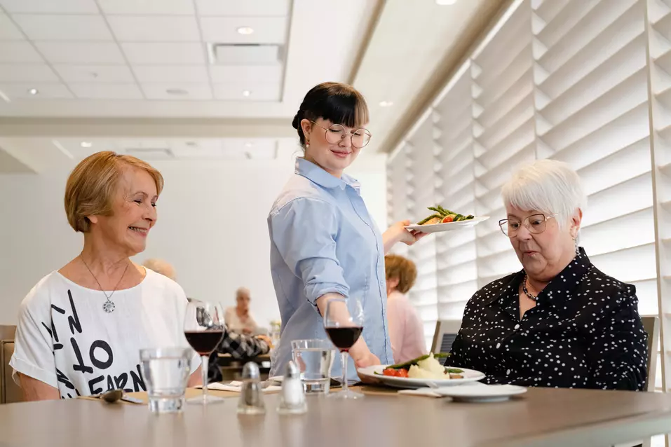 Chartwell dinning staff serving meal to the senior couple in the dinning room