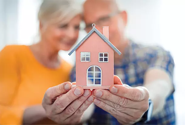 Senior couple in the background holding tiny home in the foreground