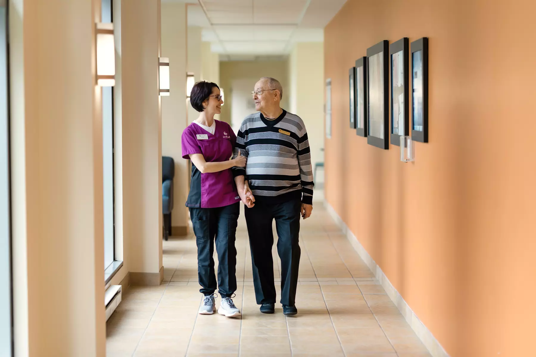 Chartwell staff is assisting senior male resident walking down an aisle / Le personnel de Chartwell aide un résident âgé à marcher dans l'allée