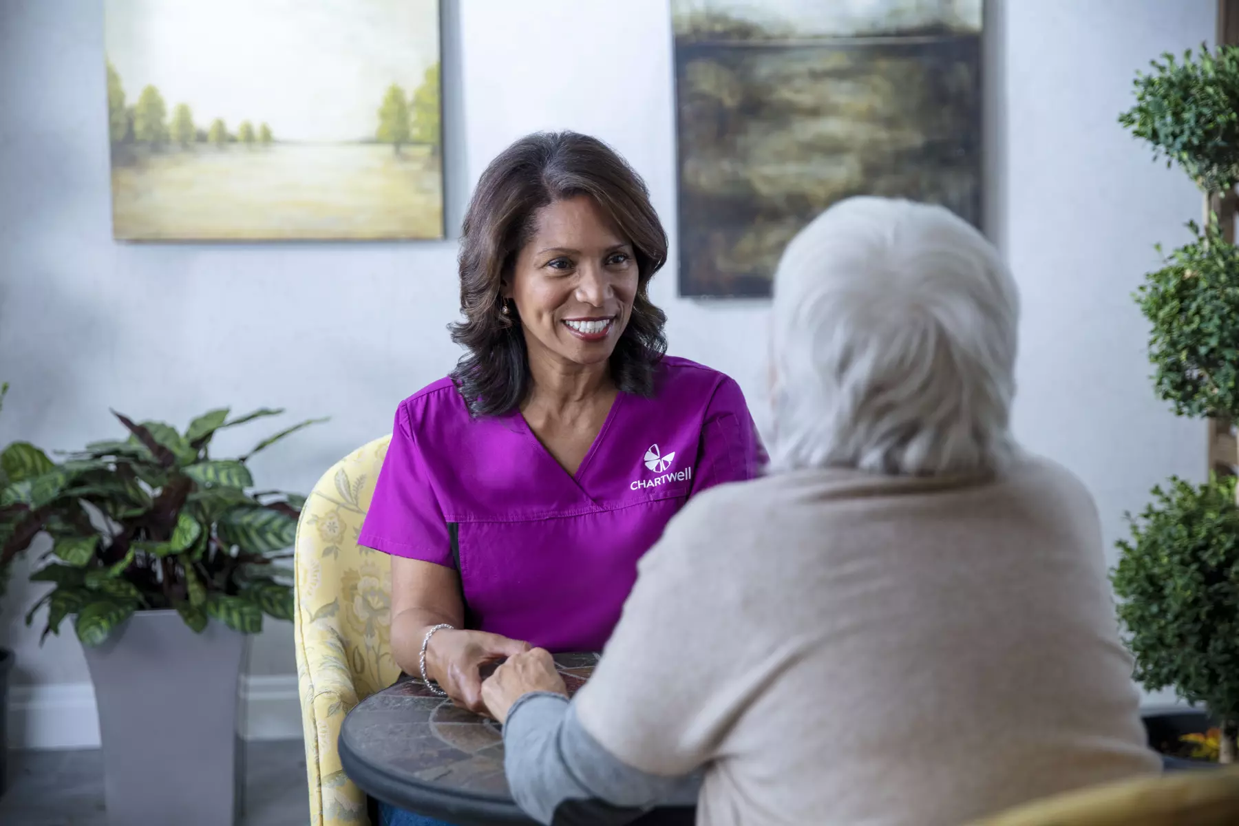 Chartwell care support staff sitting with the senior resident, holding hands smiling and having cheerful conversation.