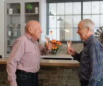 Senior men are having a joyful conversation while holding a champaign glasses in their hands / Des hommes âgés discutent joyeusement en tenant un verre de champagne à la main.