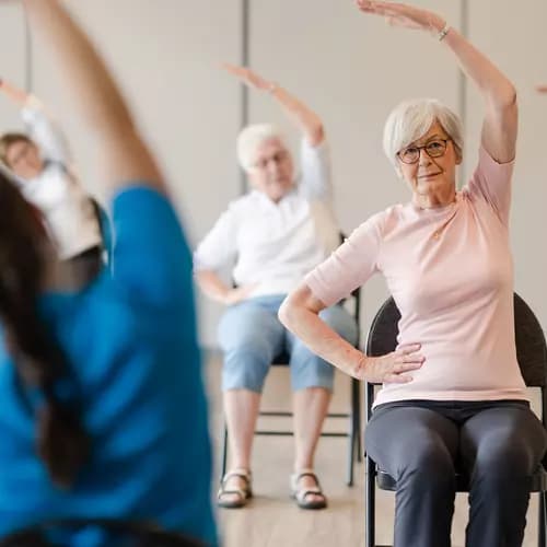 Senior residents performing chair yoga on chair with the instructor / Résidents seniors pratiquant le yoga sur chaise avec leur instructeur