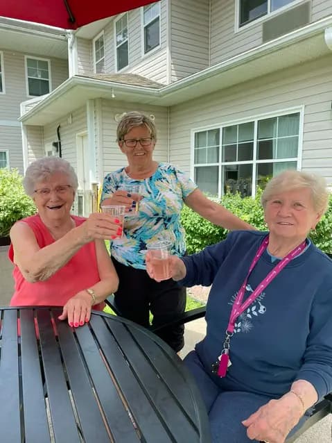 Senior women are cheering with drinks in their hands under parasol at the outdoor patio / Des femmes âgées se réjouissent, boissons à la main, sous le parasol du patio extérieur